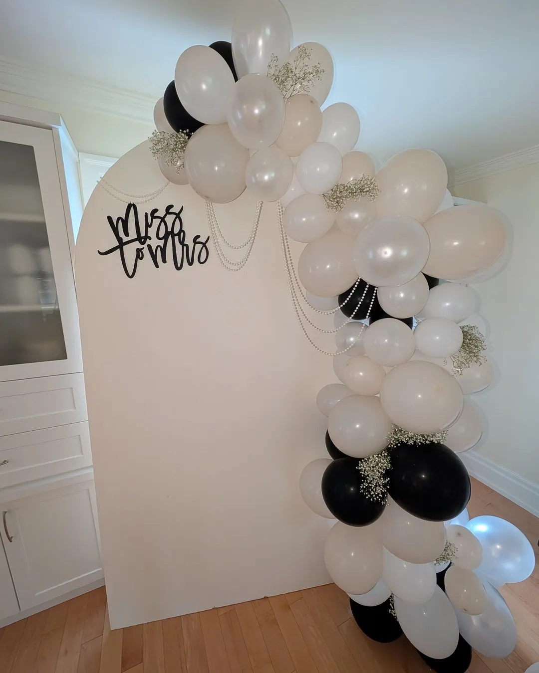 White arched backdrop with a black "Miss to Mrs" script sign and a black, white and blush balloon garland