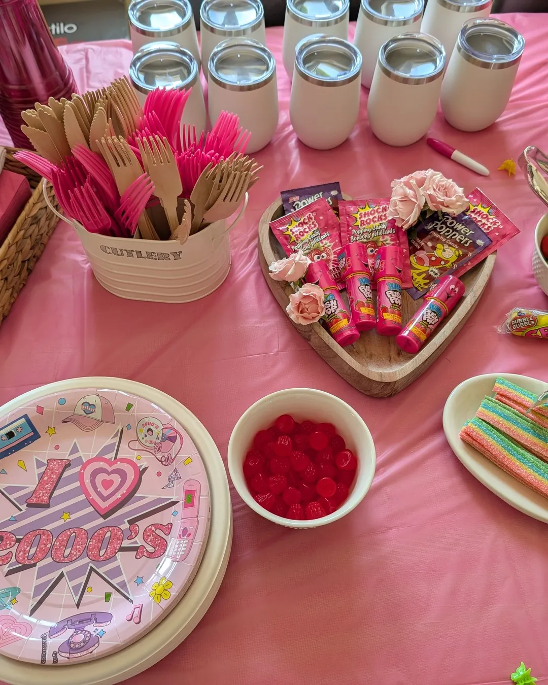 Pink party table with "I love 2000s" plates, pink cutlery, a heart tray of retro candy and white tumblers