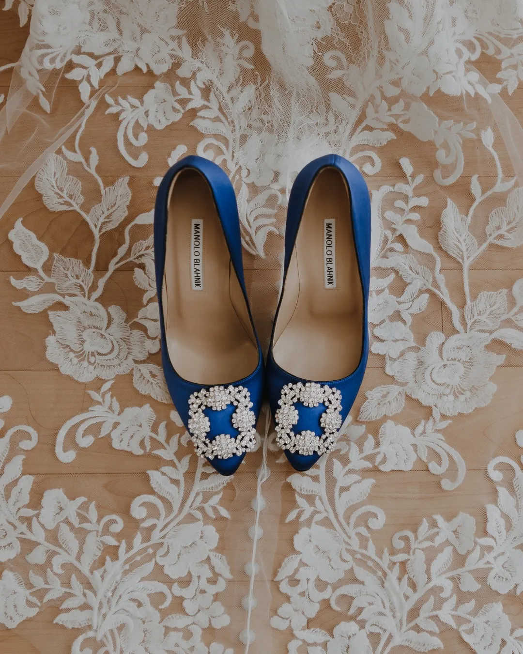 Blue satin heels with jewelled buckles resting on a lace veil
