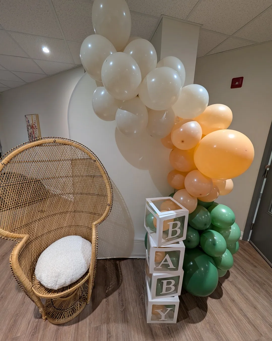 Wicker peacock chair under a cream, peach and sage balloon garland with stacked BABY blocks