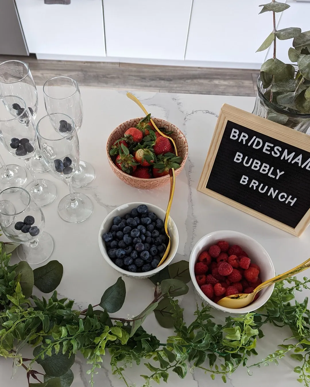 Mimosa bar with champagne flutes, bowls of berries and a "Bridesmaid bubbly brunch" letter board