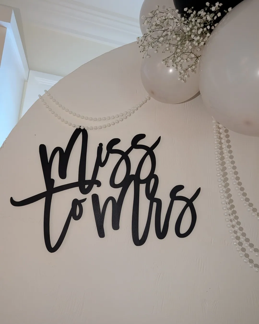 Close-up of the black script sign on the arch, draped with pearl strands and baby's breath