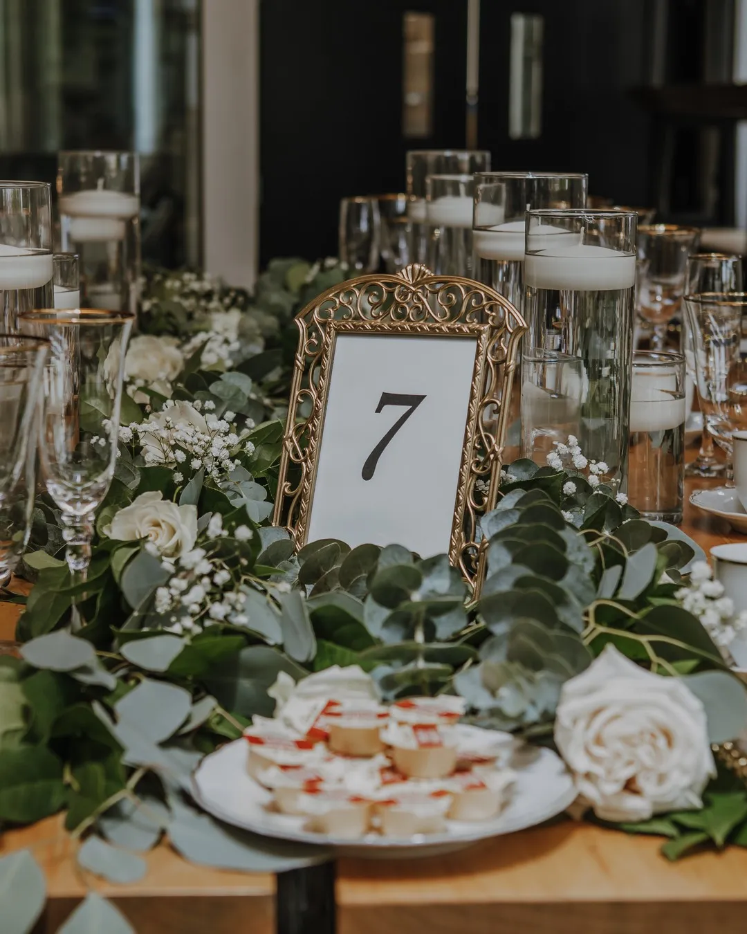 Gold-framed table number seven set in a runner of eucalyptus, white roses and baby's breath
