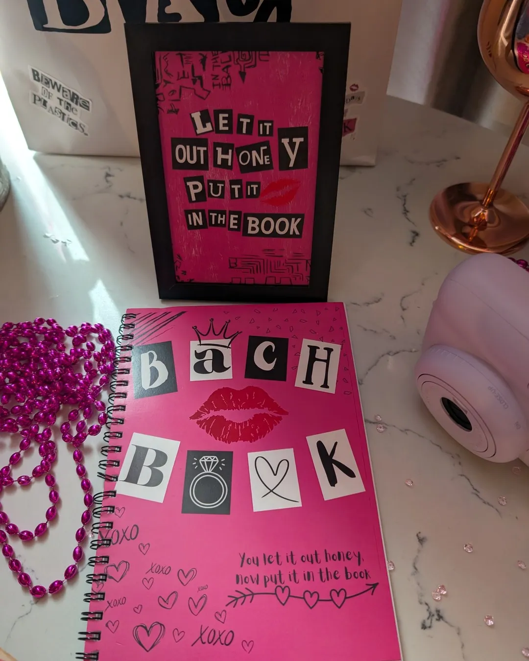 Pink "Bach book" notebook beside a framed cut-out-letter sign and pink beads