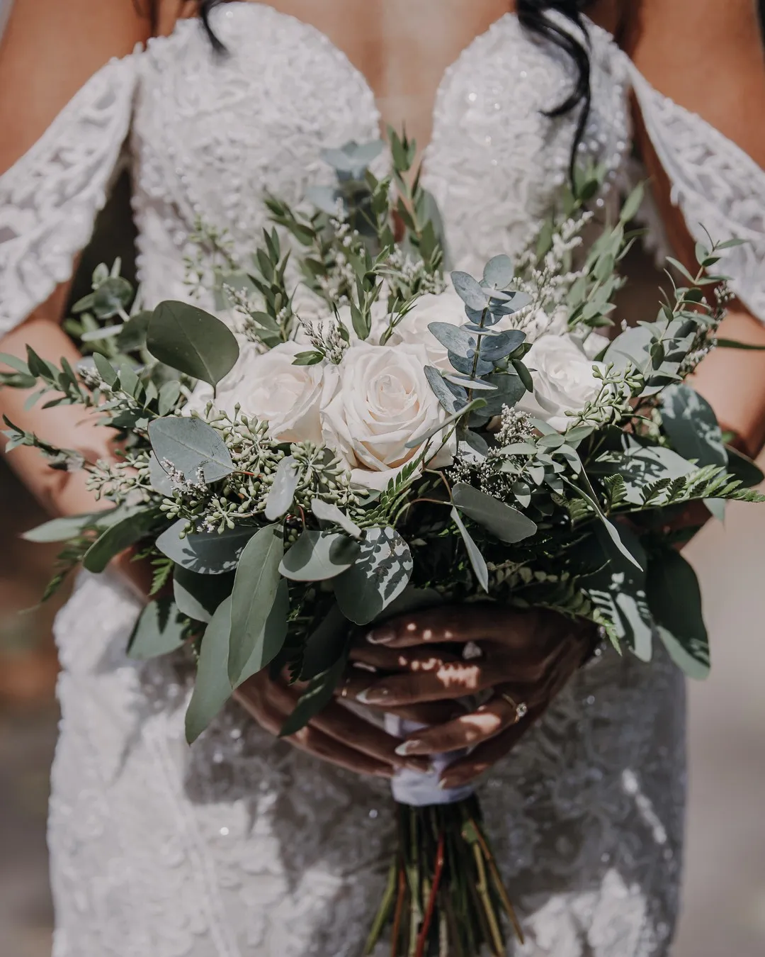 Bridal bouquet of white roses, eucalyptus and soft greenery held against a lace gown
