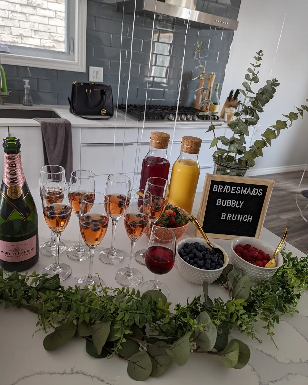 Kitchen island set with rosé champagne, juice carafes, flutes and berries along a eucalyptus garland