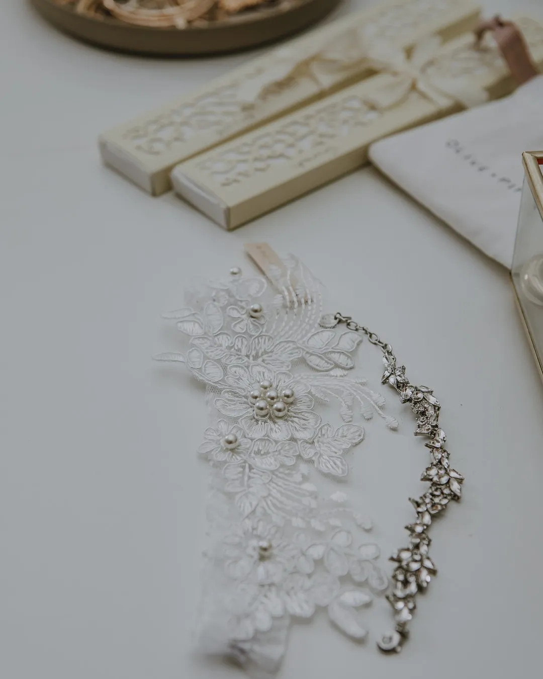 Beaded lace garter laid on a white table beside cream keepsakes