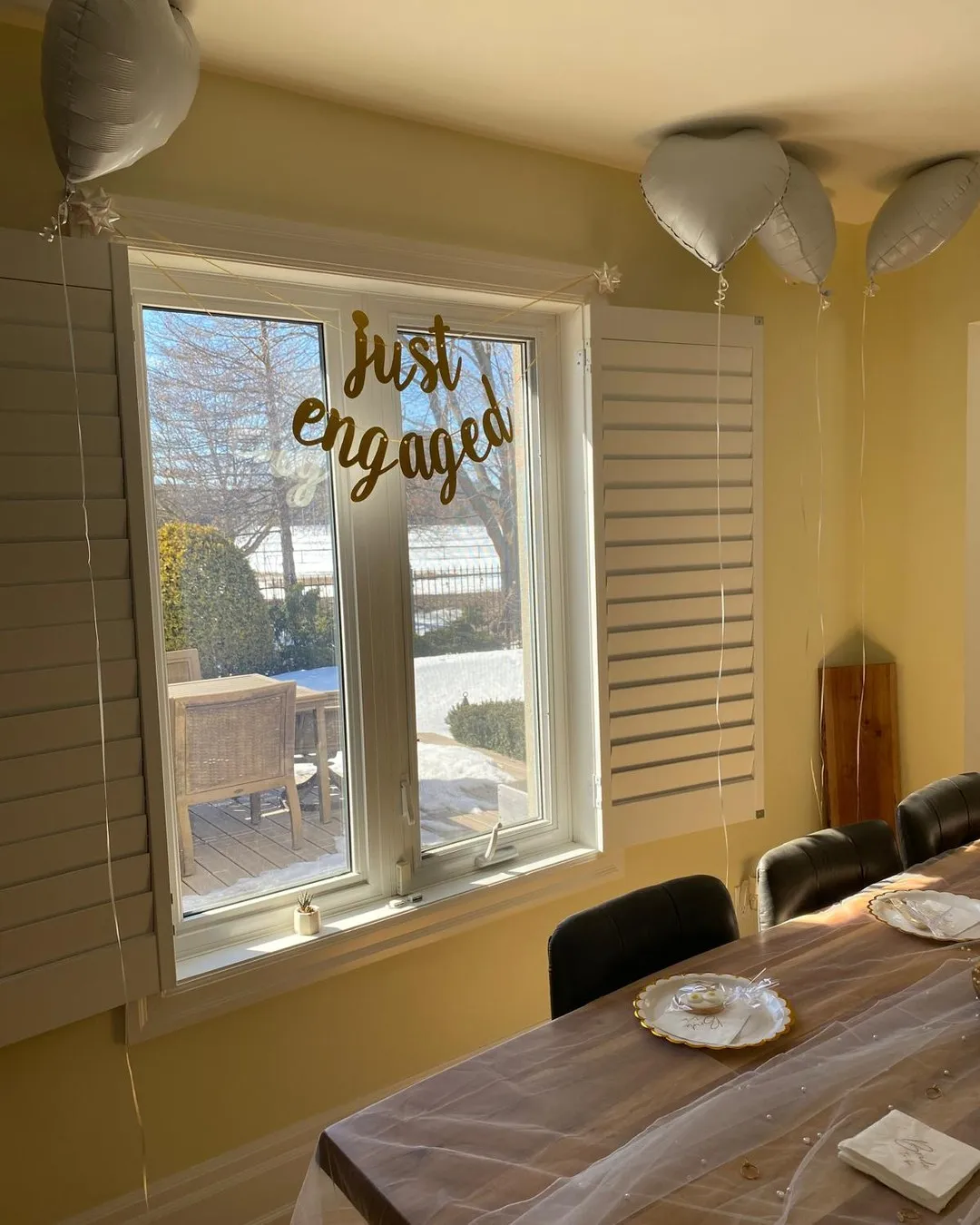 Gold "just engaged" script decal on a window above the brunch table, with white heart balloons