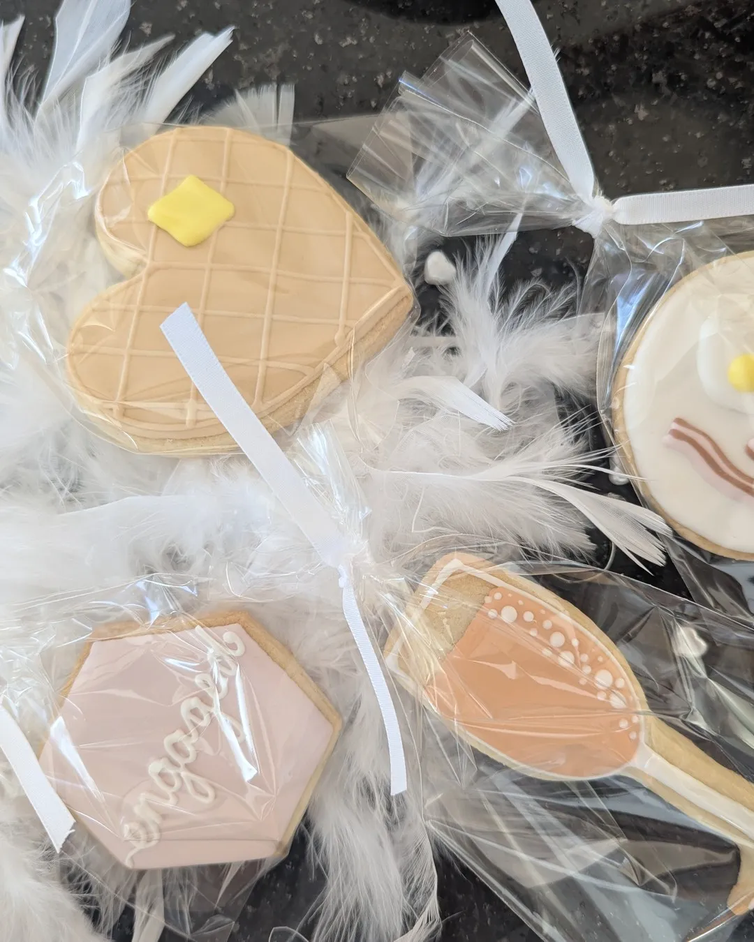Heart and ring shaped iced cookies wrapped in cellophane on white feathers