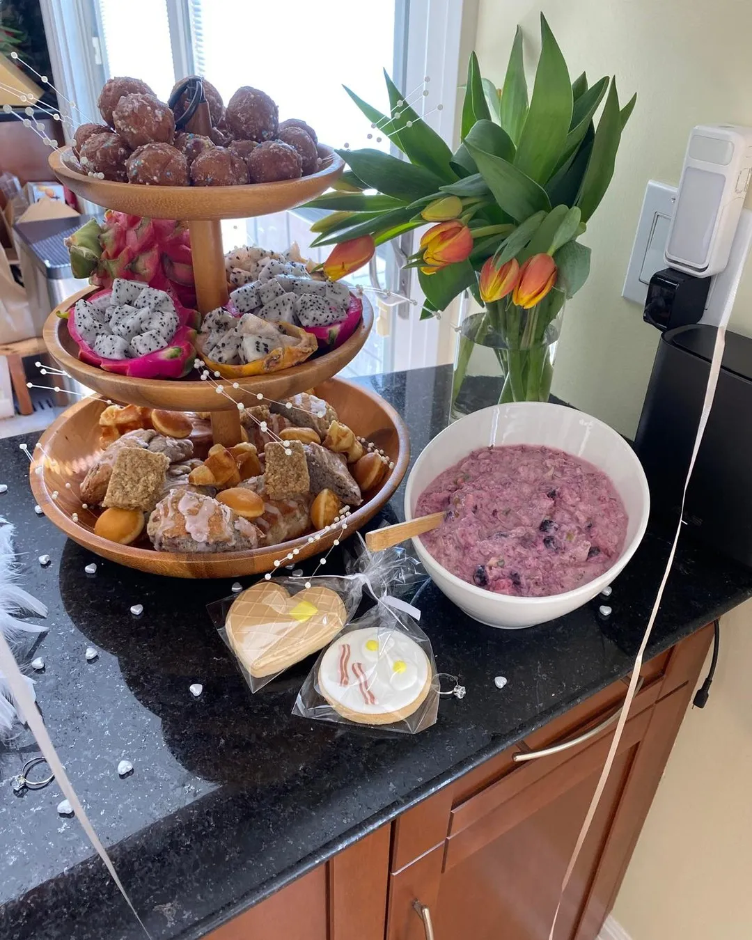 Tiered stand of doughnuts and pastries beside orange tulips and a bowl of berry dip