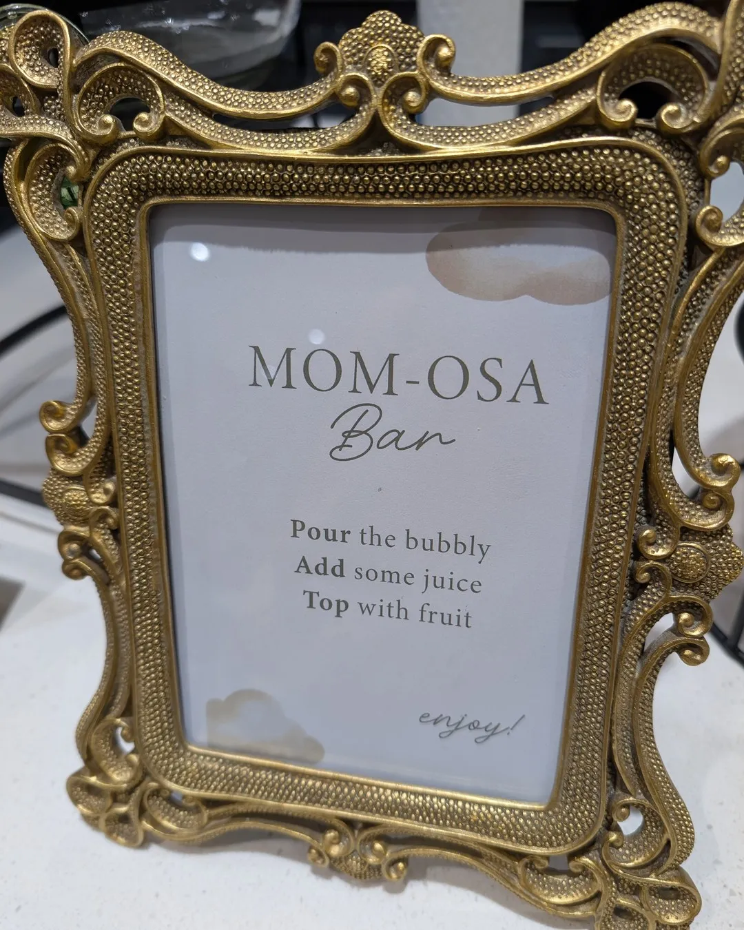 Ornate gold-framed "Mom-osa bar" sign with instructions