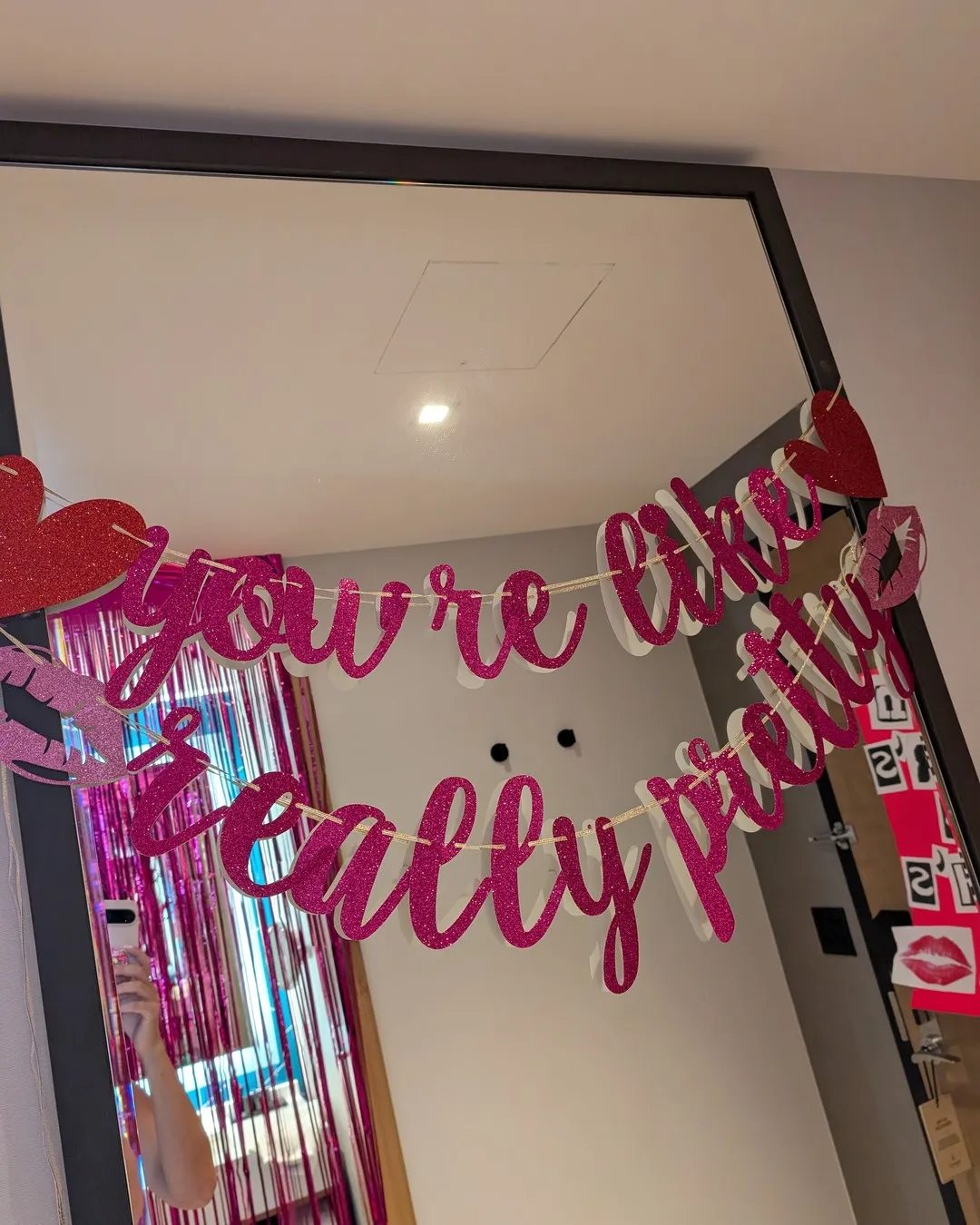 Pink script garland reading "You're like, really pretty" hung across a mirror