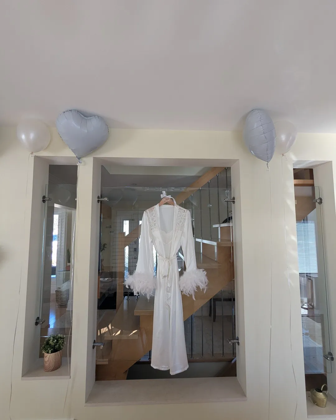 White feather-trimmed robe hanging in a doorway between silver heart balloons